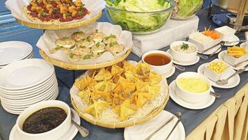Una mesa de buffet con diversos platos, incluyendo wontons fritos, ensalada y otras entradas.