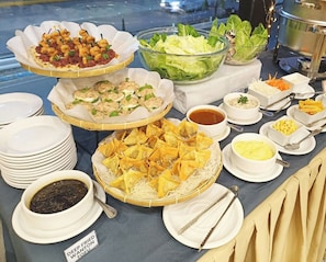Una mesa de buffet con diversos platos, incluyendo wontons fritos, ensalada y otras entradas.