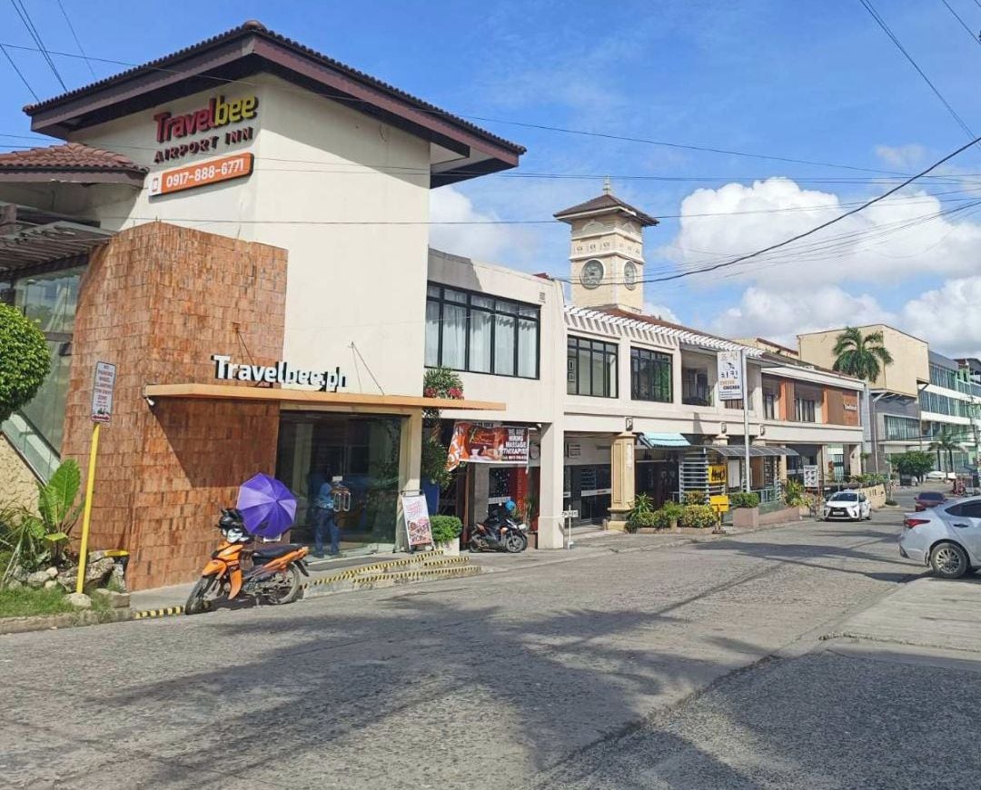 A Travelbee Airport Inn with a prominent Travelbee sign, a clock tower, and a clear view of the Marina Mall in the background.