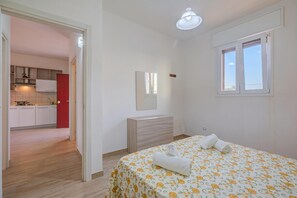 A bedroom with a bed, a bedside table, a mirror, and a window.