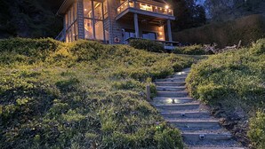A two-story wooden cabin with a balcony, surrounded by a natural landscape and a wooden staircase leading to the entrance. - Beachfront home, great for families, ocean access from yard, hot tub (Trinidad)
