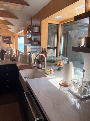 A modern kitchen with wooden cabinets, a large sink, and a view of the sea.