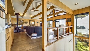 A spacious living area with a large sofa, wooden beams, and a view of the ocean through a large window. - Beachfront home, great for families, ocean access from yard, hot tub (Trinidad)