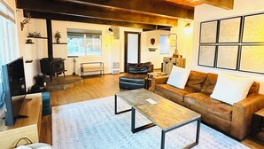 A spacious living room with a wooden ceiling, a fireplace, a sofa set, a coffee table, and a large window. - Big Bear Mountain View Cabin: Jacuzzi, Fire Pit, EV Charger (Big Bear)