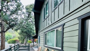 A wooden deck with four lounge chairs, a metal railing, and a building with large windows. - Big Bear Mountain View Cabin: Jacuzzi, Fire Pit, EV Charger (Big Bear)