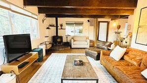 A cozy living room with a wooden ceiling, a television, a sofa, a coffee table, and a patterned rug. - Big Bear Mountain View Cabin: Jacuzzi, Fire Pit, EV Charger (Big Bear)