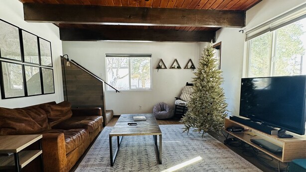A living room with a wooden ceiling, a brown leather sofa, a coffee table, a television, and a Christmas tree. - Big Bear Mountain View Cabin: Jacuzzi, Fire Pit, EV Charger (Big Bear)