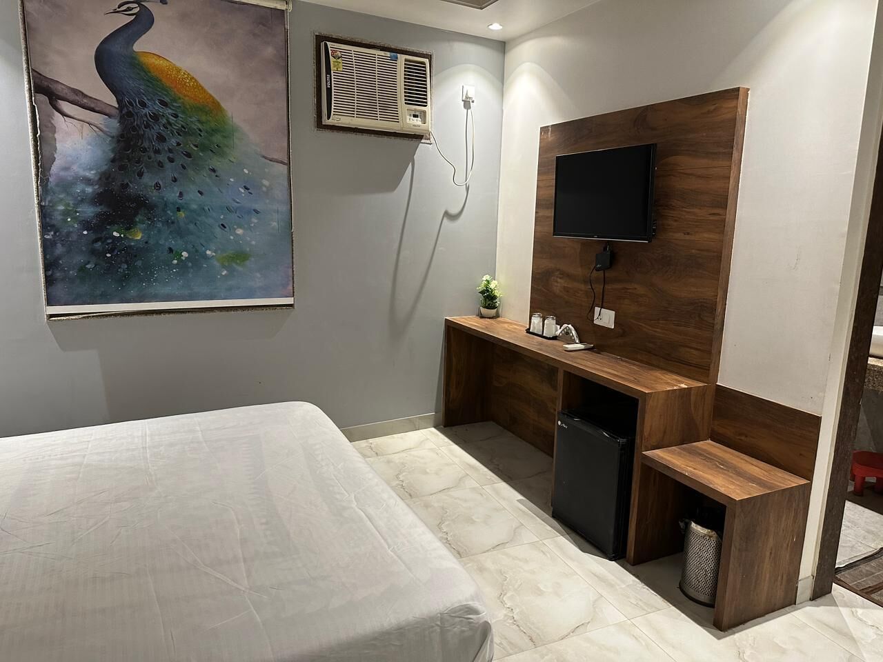 A bedroom with a bed, a desk with a TV, and a peacock painting.