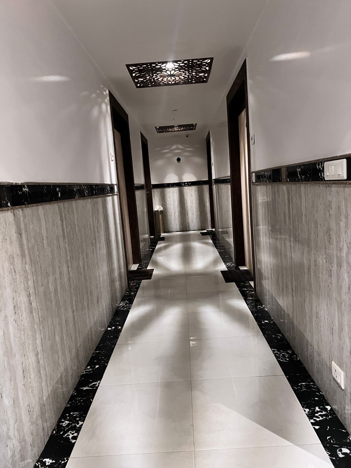 A long, narrow hallway with marble flooring and walls, featuring a central light fixture and doors on either side.