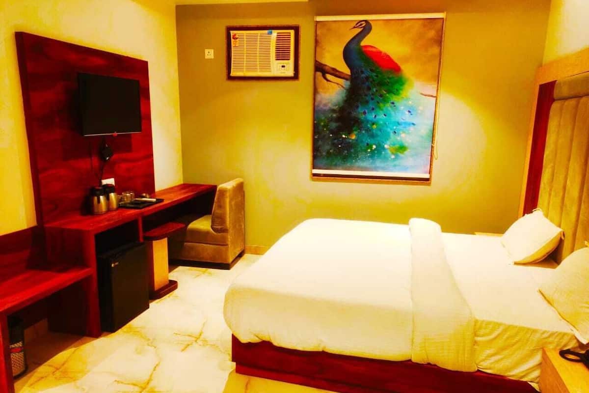 A hotel room with a bed, a desk, a chair, a television, and a peacock painting on the wall.