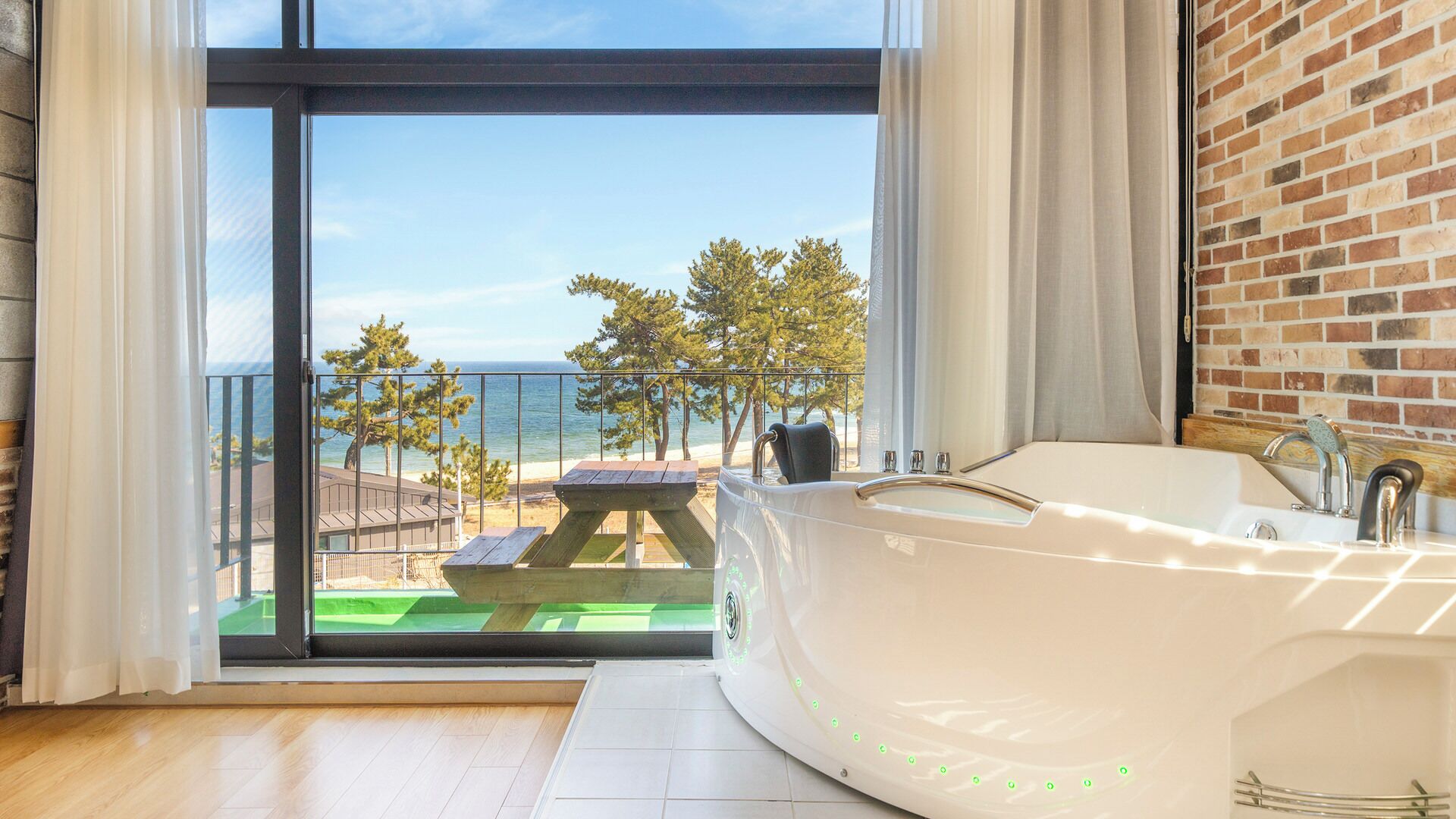 A modern bathroom with a large bathtub, a view of the beach, and a wooden deck outside.