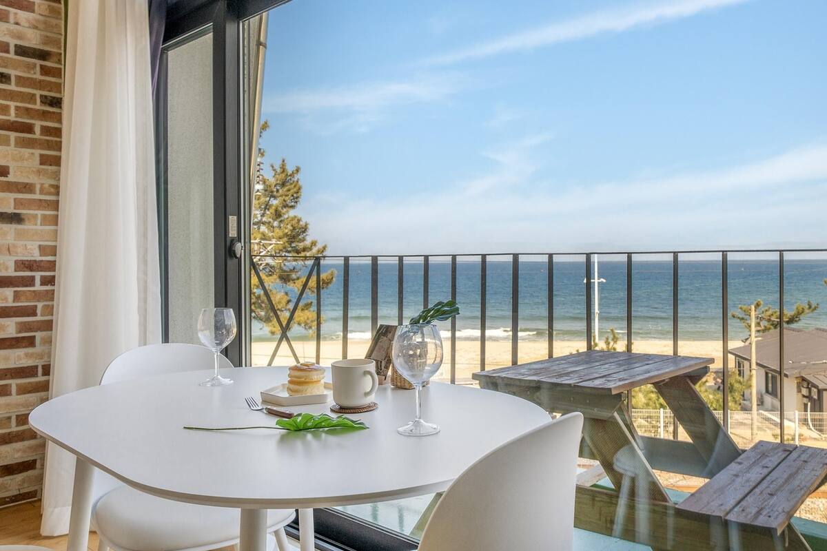 Een balkon met een tafel voor twee personen, met uitzicht op een strand en de oceaan.