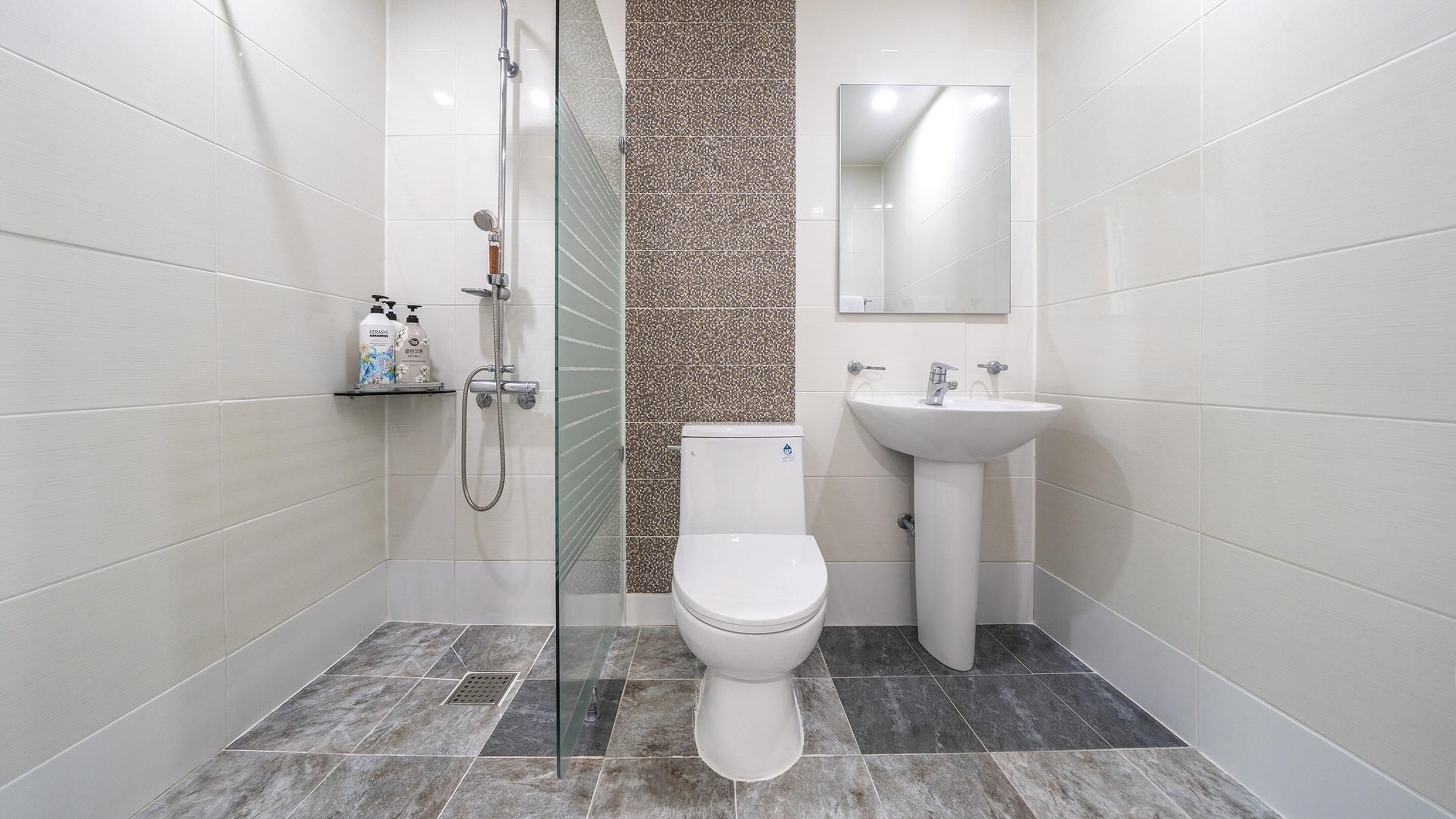 Un baño moderno con ducha de vidrio, inodoro blanco y lavamanos sobre pedestal.