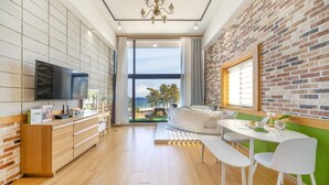 A modern kitchen with a large TV, wooden cabinets, and a view of the beach. - Gangneung Jd38 spa Pension (Gangneung)
