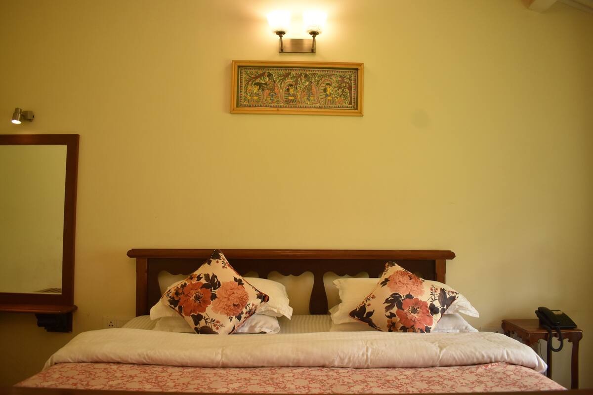 A neatly made bed with floral pillows, a wooden headboard, and a wall-mounted light fixture above.