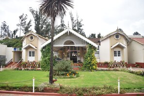 A building with a symmetrical facade, a central entrance with a decorative arch, and a well-maintained garden with potted plants and flowers. - THE GRANGE HOTEL (Ootacamund)