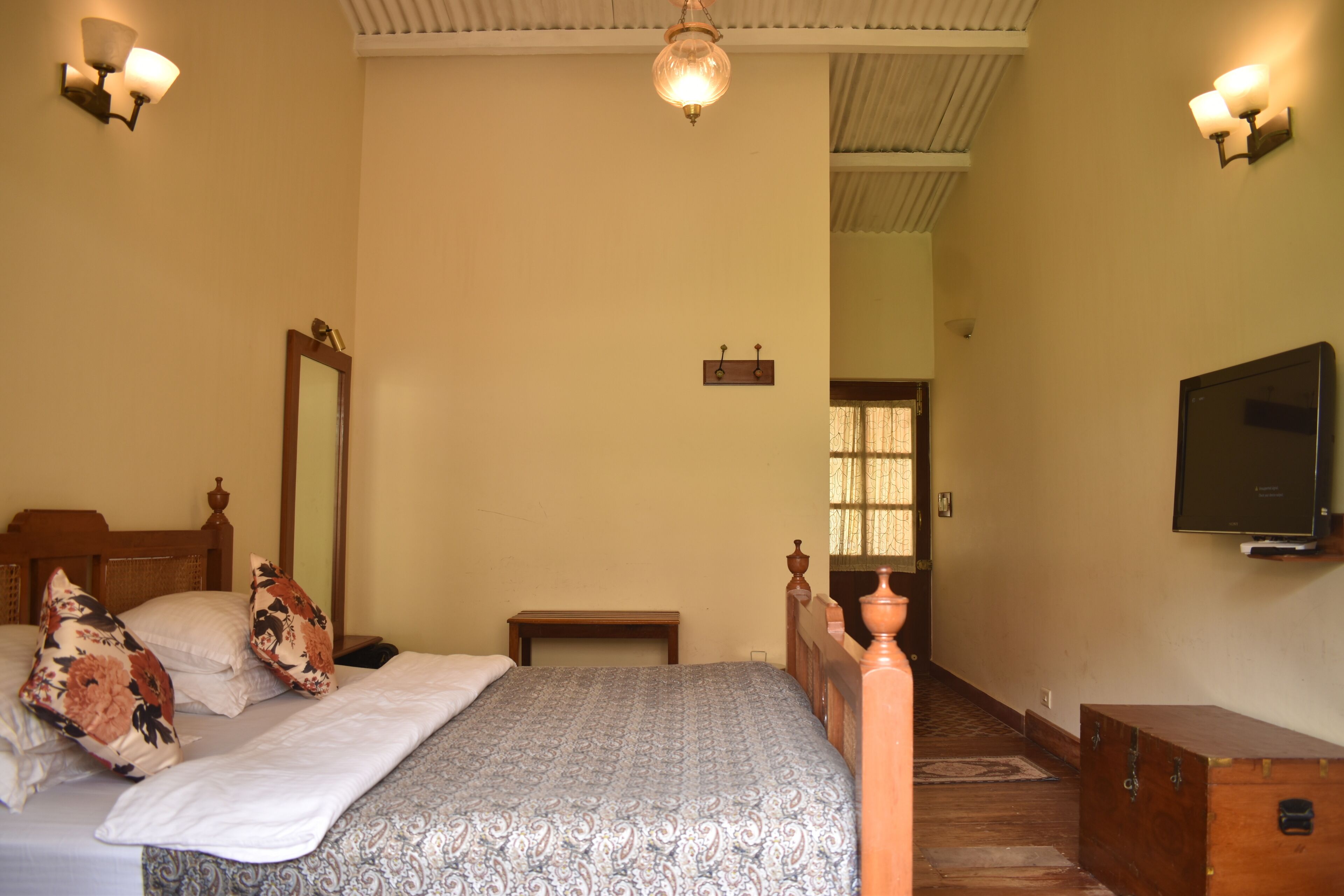 A bedroom with a bed, a wooden headboard, a mirror, a television, and a wooden chest of drawers.