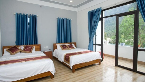 A hotel room with two beds, a wooden floor, and a large sliding glass door leading to a balcony. - Nam Anh Hotel (Phong Nha)