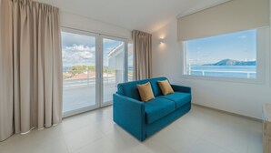 Ein modernes Wohnzimmer mit einem blauen Sofa, großen Fenstern und Meerblick.