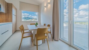 A modern kitchen with wooden cabinets and a dining area with a table and chairs. There is a window with a view of a cityscape and a balcony with a railing. - RESIDENCE PADULELLA - 2 - RESIDENCE PADULELLA - ATTICO SX (Portoferraio)