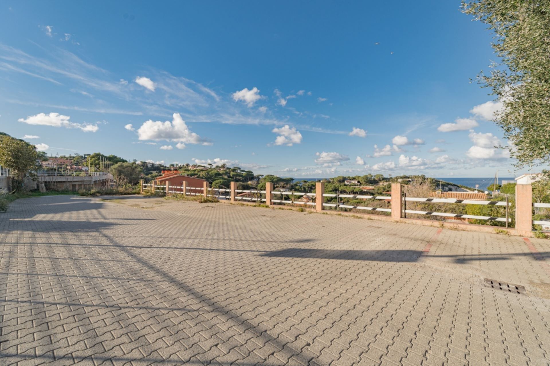 A paved area with a fence, a building, and a view of a coastal landscape.