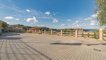 A paved area with a fence, a building, and a view of a coastal landscape.