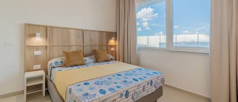 A bedroom with a bed, bedside tables, a wooden headboard, a window with curtains, and a view of the sky.