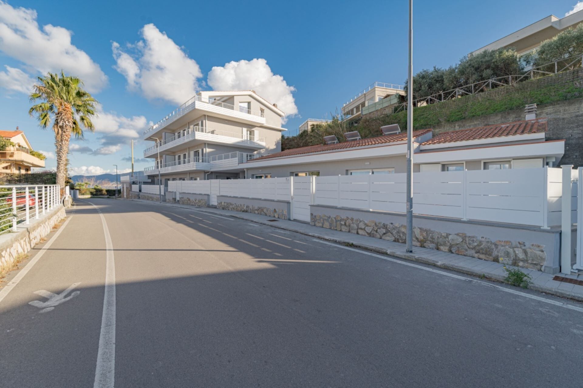 Una carretera costera con edificios modernos, una palmera y cielo despejado.