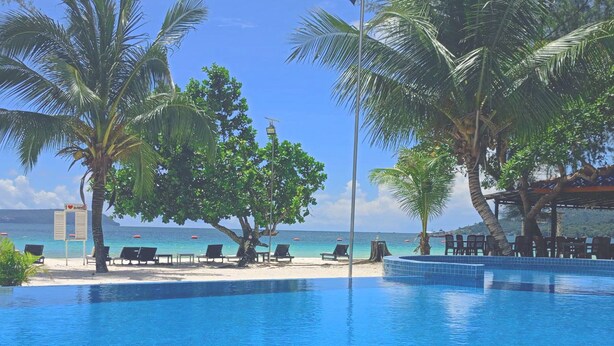 A clear blue pool with lounge chairs and palm trees, overlooking a beach with umbrellas. - SCARLET SAILS VILLA (Koh Rong)