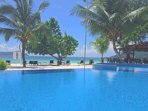 A clear blue pool with lounge chairs and palm trees, overlooking a beach with umbrellas. - SCARLET SAILS VILLA (Koh Rong)