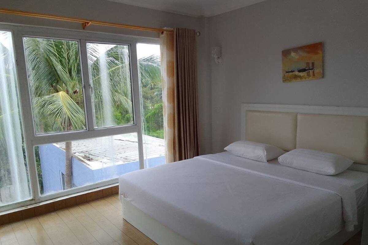 A bedroom with a large bed, a window with curtains, and a painting on the wall.