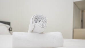 Een keurig opgevouwen witte handdoek op een bed in een hotelkamer.