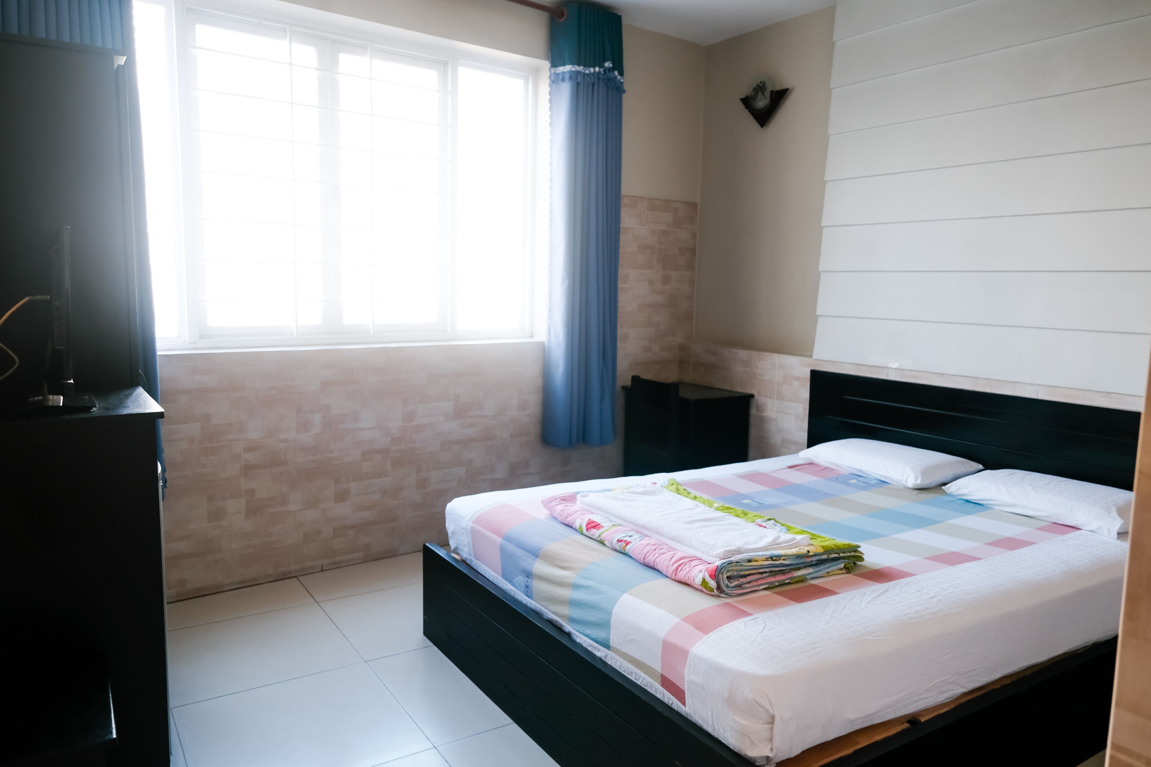 A neatly made bed with a checkered bedspread, a bedside table, and a window with curtains.