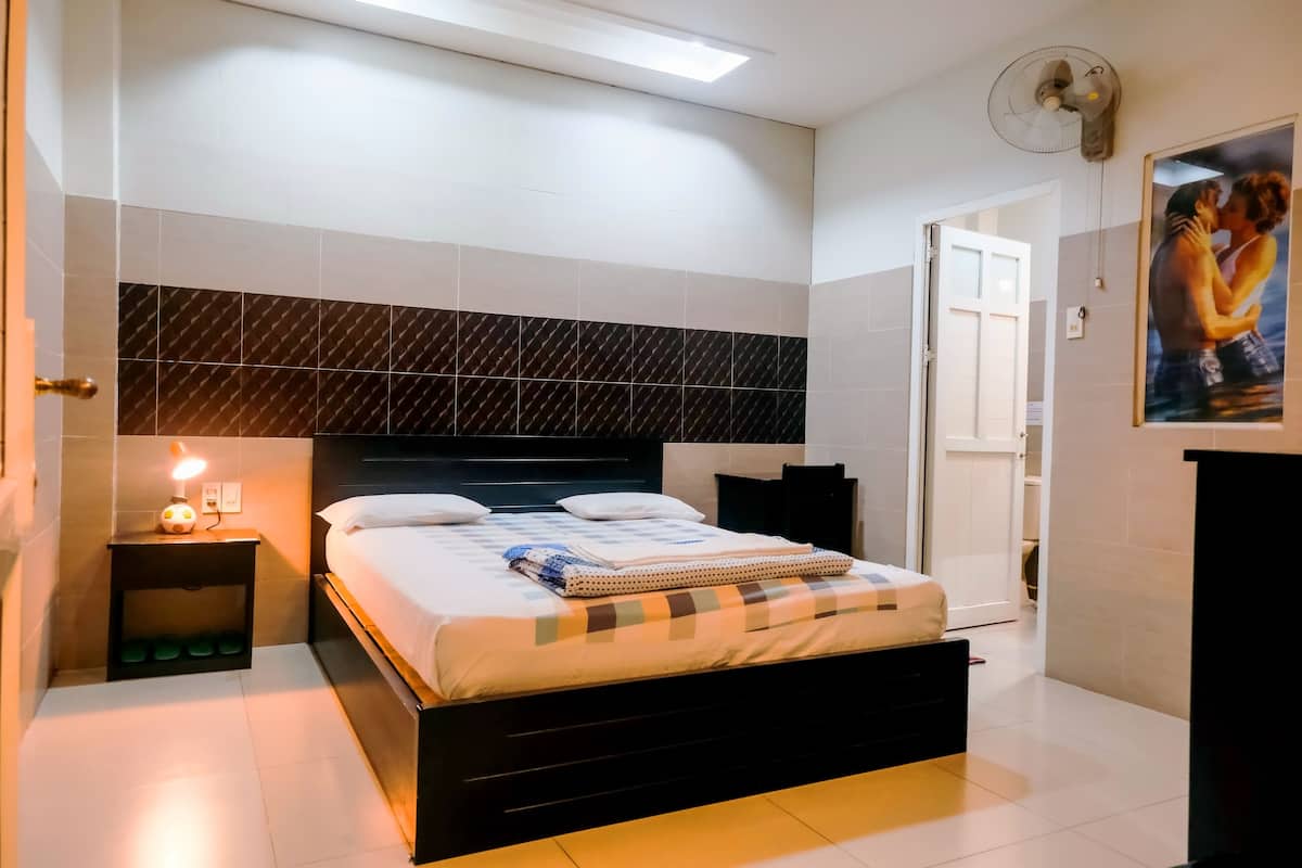 A modern bedroom with a bed, bedside tables, a wall-mounted fan, and a door leading to another room.
