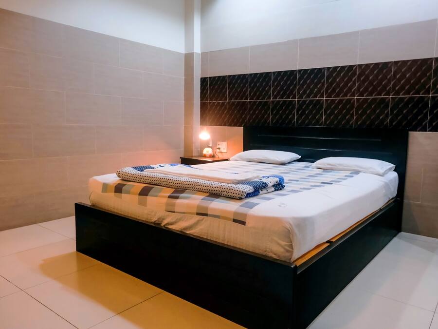 A neatly made bed with a checkered blanket, a bedside lamp, and a dark headboard.
