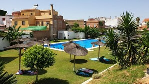 Una piscina con sombrillas de paja, un área verde y un edificio con fachada amarilla.