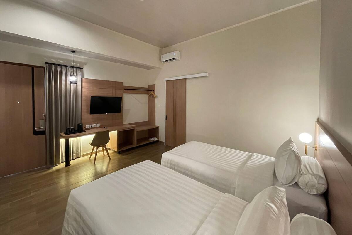 A hotel room with two beds, a desk with a chair, a TV mounted on the wall, and a wardrobe.