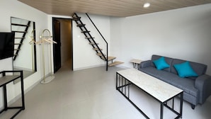 A modern living room with a grey sofa, a coffee table, a TV mounted on the wall, and a wooden staircase. - Azana Essence Sanggabuana Bogor (Bogor)