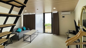 A modern interior with a staircase, a sofa, a table, and a view through a glass door. - Azana Essence Sanggabuana Bogor (Bogor)