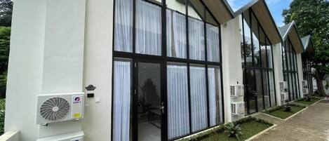 A modern building with large windows, air conditioning units, and a paved walkway with small planters.