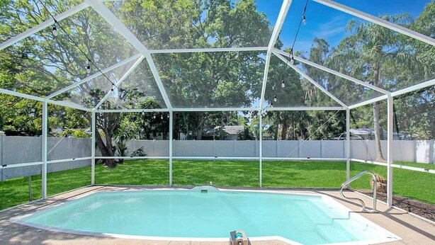 Una piscina con cerramiento de vidrio, rodeada de césped y árboles.