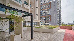 Ett modernt utomhusområde med ett klinkergolv, planteringslådor med små träd och en röd gångväg.