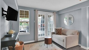 A living room with a sofa, a round mirror, a television, and a window with blinds. - The Marlin House: Waterfront Escape with Dock, Outdoor Kitchen & Stunning Views! (Willis)