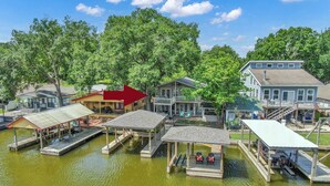 A waterfront property with multiple docked boats, a covered dock area, and a house with a balcony overlooking the water. - The Marlin House: Waterfront Escape with Dock, Outdoor Kitchen & Stunning Views! (Willis)