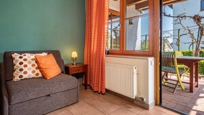A room with a sofa, a table, a chair, a lamp, and a window with curtains. - Room 'Kräutergärtle' with Private Terrace, Shared Garden and Wi-Fi (Immenstaad am Bodensee)