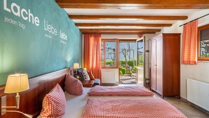 A hotel room with a bed, checkered pillows, a lamp, a view of the outdoors, and a wall with text. - Room 'Kräutergärtle' with Private Terrace, Shared Garden and Wi-Fi (Immenstaad am Bodensee)