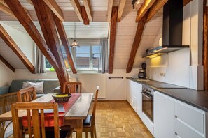 A kitchen with wooden beams, a dining area with a table and chairs, and a view through a window.