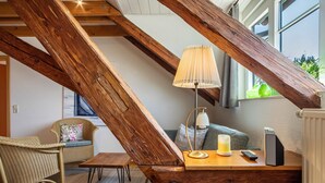 Una habitación acogedora con techo inclinado, un escritorio de madera con lámpara, una silla y un sofá.