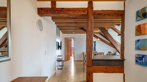 Techo de madera con vigas a la vista, un banco de madera, una mesa de comedor y vista a un pasillo que conduce a una puerta.