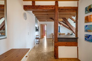A wooden ceiling with exposed beams, a wooden bench, a dining table, and a view of a hallway leading to a door.